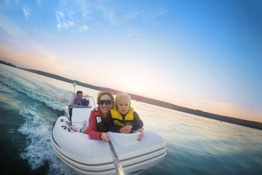 Happy Couple With Daughter Riding Boat On Lake Or River At Sunset. Pair  With Child Making Selfie While Water Activity.  Happy Family  Recreation And Adventure Concept. Beautiful Travel Background