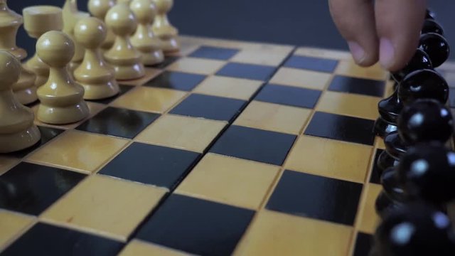 Panning shot of a chess board with a hand moving the chess pieces.