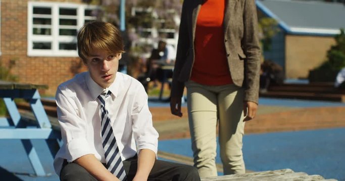 4K Kind teacher comes to talk to sad lonely boy outdoors in the school yard. Slow motion