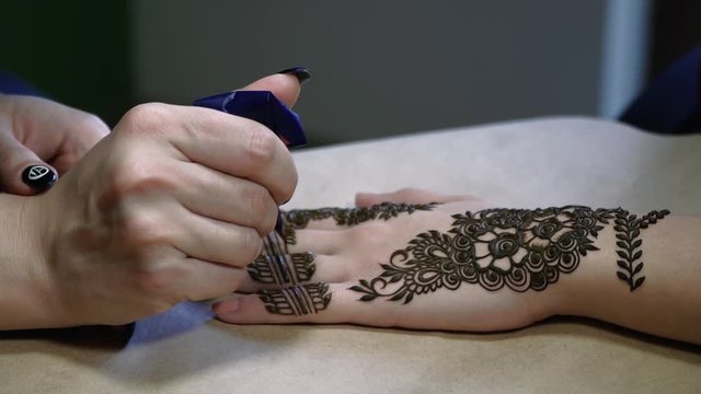 An caucasian lady does a henna tattoo on a client's hand and wrist.