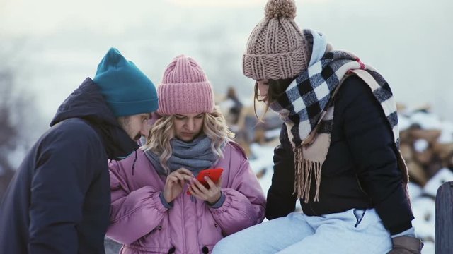 three friends standing online content digital modern smart phone outside street winter cold weather warm clothes hipster stylish girls woman man touching screen laughing smile happy walk holidays