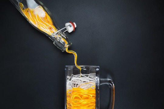 Pouring strings from bottle to beer glass mug against black background abstract minimalistic concept.