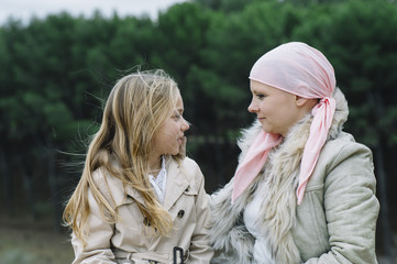 A woman with cancer is  next to her daughter. A girl is hugging a woman happy