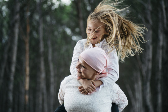 A woman with cancer is  next to her daughter. A girl is hugging a woman happy
