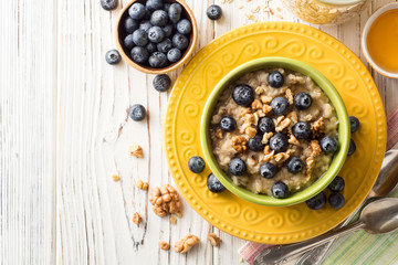Oatmeal porridge with blueberries, walnuts and honey on white wooden background.