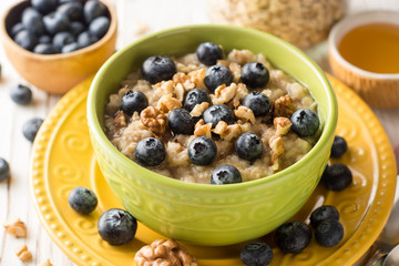 Oatmeal porridge with blueberries, walnuts and honey on white wooden background.