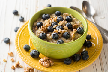 Oatmeal porridge with blueberries, walnuts and honey on white wooden background.