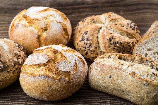 Different kinds of fresh bread on wooden table. Isolated assortment of bread on brown background.