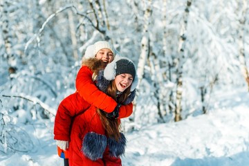 Beautiful teenage girls having fun outside in a wood with snow in winter on a wonderful frosty sunny day. Friendship and active life consept