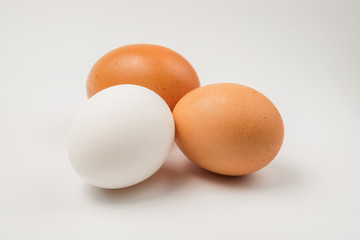 Two brown and single white chicken eggs on a white surface.