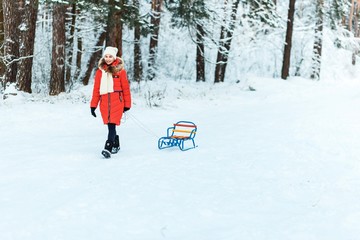 A girl  with sledge. Beautiful teenage girl in red down jacket having fun outside in a wood with snow in winter on a wonderful frosty sunny day. active life consept