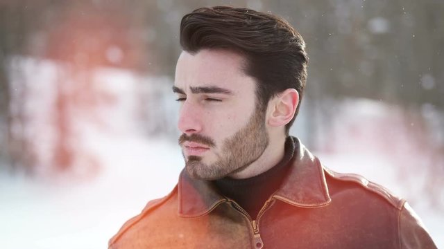 Stylish man walking confidently looking away on territory of contemporary winter resort covered in snow in the mountain