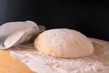 Aluminum scoop with flour and dough on wooden Board on black background