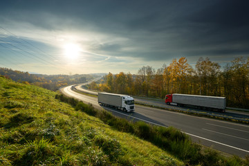 Trucks driving on the highway turning towards the horizon in an autumn landscape with sun shining...