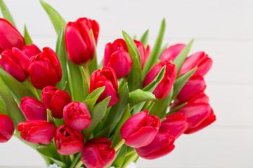 Fresh red tulip flowers bouquet on shelf in front of wooden wall.