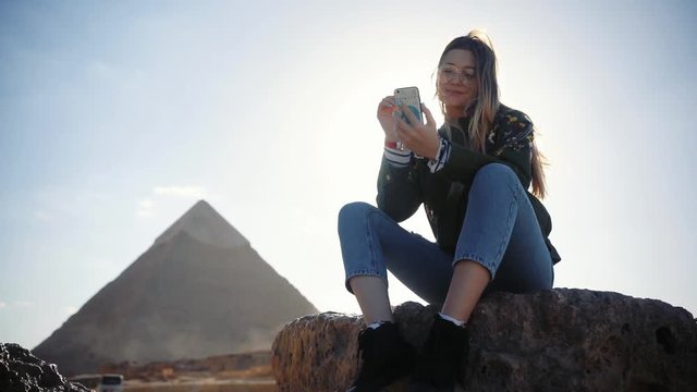 Attractive young woman use phone smile near Giza pyramids, Egypt sunlight ancient happy tourist travel africa arab culture mobile architecture adventure archeology cairo connect portrait beautiful