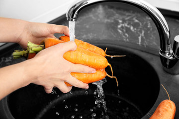 Young woman washing fresh raw carrot in kitchen