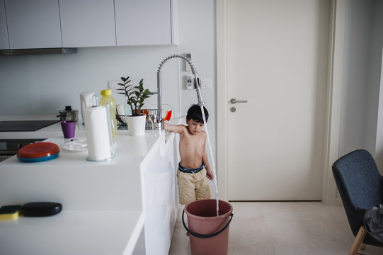 Shirtless Boy Filling Water In Bucket At Home