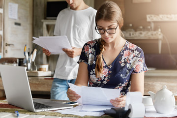 Beautiful woman reads documents attentively, prepares financial report, calculates figures and...