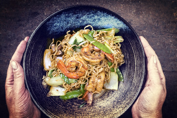 Traditional stir-fried Thai phat phak kung with mie noodlesas top view in a bowl in woman hands