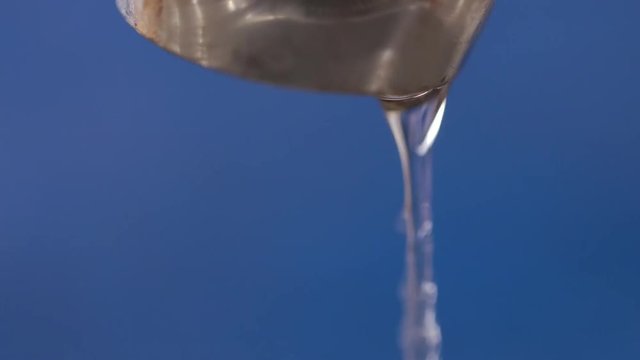 A macro of dripping kitchen faucet spout, water waste. Blue background.