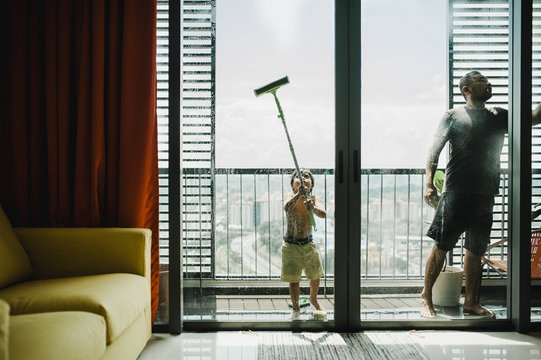 Father and son cleaning windows in balcony seen through glass