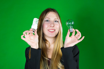 Serious pretty business woman holding a light bulb on a green background. Close-up face model with two kinds of light bulbs. Concept of saving money for electricity