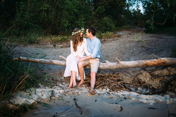 Smiling couple sitting on a log by the sea and looking at each other with love