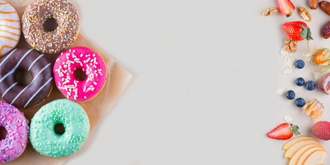 Colorful sweet doughnuts with different kinds of topping and fruits on light stone background with place for text.