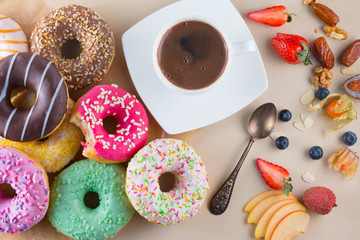Many sweet donuts with cup of aroma coffee, fruits and one bitten pink doughnut on light stone background.