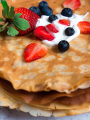 Side view of stack of thin pancakes poured with sour cream and decorated with fresh strawberries and blueberries. The concept of Russian holiday Maslenitsa, Shrovetide