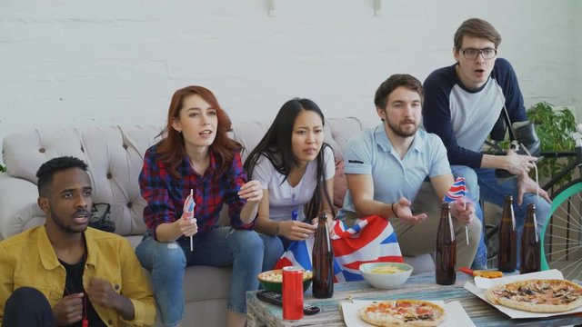 Group of young friends sports fans with British national flags watching sport championship on TV together and happy about winning favourite team at home