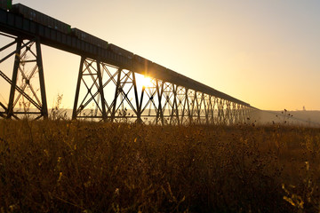Sunrise glinting through steel trusses of a steel train bridge
