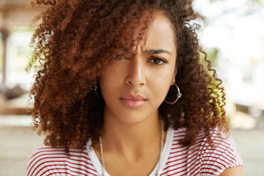 Close up portrait of puzzled discontent female with dark pure healthy skin and frizzy hair, looks in bewilderment at camera, expresses her disagreement and discontent. Embarrassed African woman