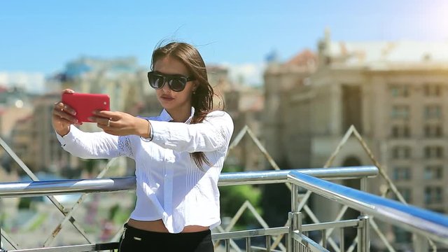 Attractive girl in sunglasses with red cell phone. Businesswoman makes selfie on his smartphone. Woman makes photos on mobile phone