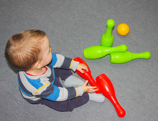 Baby and bowling. A little boy is sitting on the floor with skittles. Bowling game, a child throws a ball