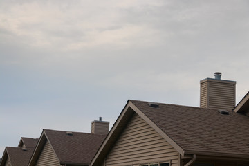 Detail of plain, beige suburban rooftops with cloudy sky.