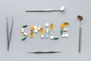 Prevention of diseases of the oral cavity. Healthy smile. Dentist appointment. Word smile lined with pills near dentist tools. Grey background top view