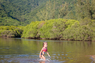 Young cute little girl playing in the water in a beautiful river on a sunny summer day