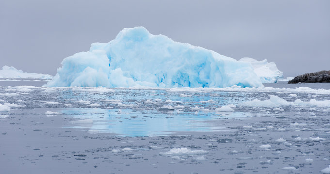 Cierva Cove Iceberg with overcast skies above and the gray water of the Southern Ocean with sea ice in the foreground.