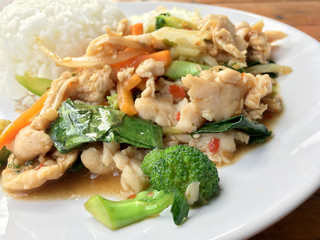 stir-fried chicken with mixed vegetables and fried egg in thai style with rice in white dish on old wooden table. Asian thai food.