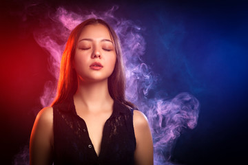 Asian dark-haired woman in a black dress posing against a background of red and red smoke from a vape on a black isolated background