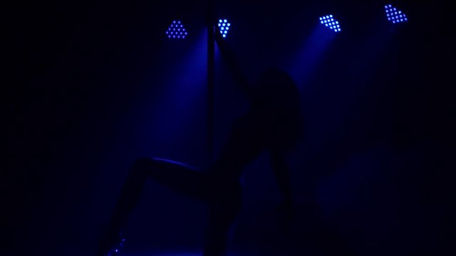 Luxurious sexy girl dancing on a pole in the dark in the light of blue professional lamps. Pole dance.
