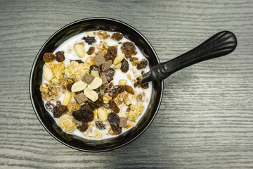 A spoon in a bowl with crunchy toasted muesli with peanuts, milk chocolate, caramel and raisins with milk. View from above.