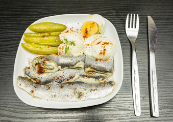 White plate with marinated herring in oil, boiled hard-boiled egg, cucumber and mayonnaise....