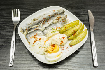 Breakfast or brunch. Plate with marinated herring in oil, boiled hard-boiled egg, cucumber and mayonnaise and sprinkled with spices such as black pepper and red paprika.