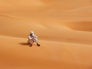 Fototapeta na wymiar Desert in Africa, a wanderer sits on sand dunes in Arab clothing.