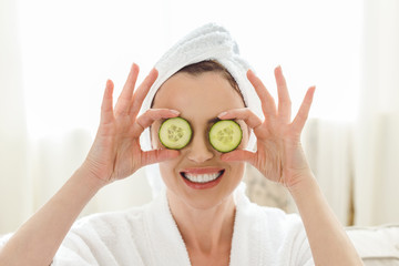 smiling woman holding cucumber slices in front of eyes