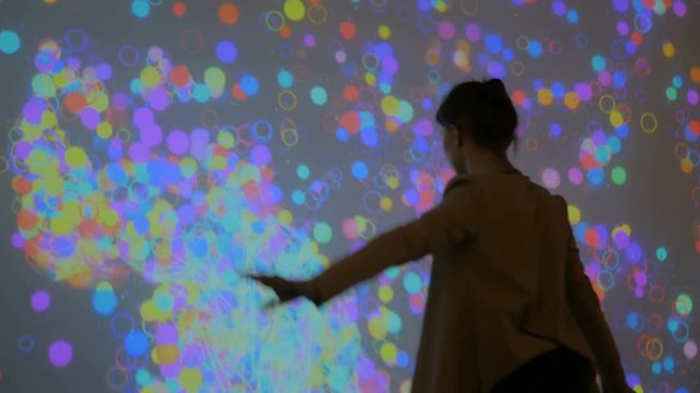 Large screen augmented reality experience - woman waving her arms in front of display. Science, future and technology concept
