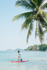 Beautiful girl on stand up paddle board on sea at tropical resort